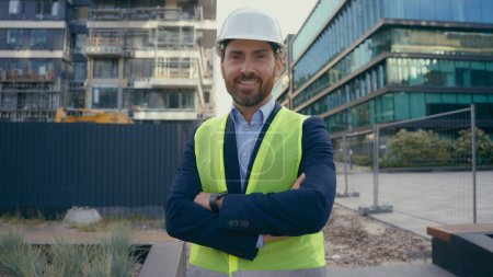 Photo for Smiling Caucasian middle-aged adult man worker in hardhat happy smile contractor engineer in helmet vest portrait builder architect hands crossed inspector of city urban building construction industry - Royalty Free Image