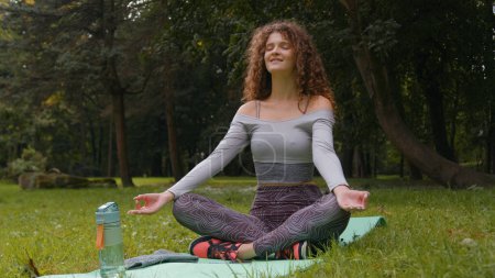 Téléchargez les photos : Femme caucasienne sportive athlète yogi femme fille assise en position lotus méditation en plein air dans le parc nature calme pleine conscience méditation pose yoga tranquille en plein air pratique méditation harmonie zen - en image libre de droit