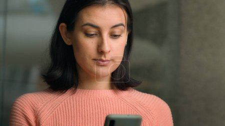 Photo for Close up Caucasian woman 20s lady female girl indoors in office shopping mall scrolling phone looking at mobile screen buying online browsing smartphone. Businesswoman look at telephone chat website - Royalty Free Image