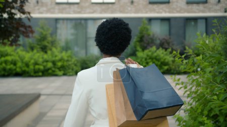Photo for Back view from behind walking in city outdoors African American woman turning looking at camera happy smiling shopper girl female buyer customer lady client walk with shopping bags purchases discounts - Royalty Free Image