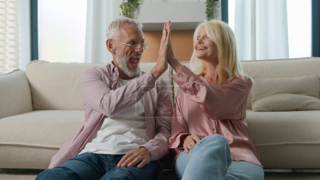 Photo for Caucasian smiling family couple man woman grandparents working remote on floor in living room at home using computer application check email closing laptops high five celebrating success job well done - Royalty Free Image
