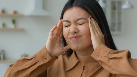 Téléchargez les photos : Fatigué malade femme asiatique se sentent mal à la tête douleur massage temples toucher mal à la tête grimace souffrir de migraine blessé hypertension artérielle fille coréenne malade femme d'affaires chinoise dans la cuisine - en image libre de droit