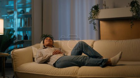 Téléchargez les photos : Femme afro-américaine fatiguée dans la nuit du soir salon couché sur un canapé confortable tombant sur un canapé doux confortable détendu calme tranquille fille rêve repos à la maison détente stress week-end libre loisirs - en image libre de droit