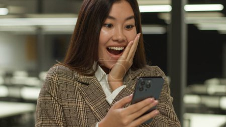Photo for Asian girl in office Korean business woman lady Chinese businesswoman Japanese female manager worker employer student shock amazed wow surprised with mobile phone good amazing news achieve win triumph - Royalty Free Image