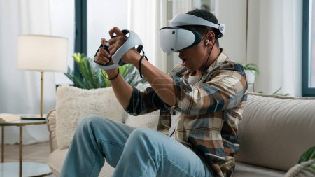 Téléchargez les photos : Afro-Américain lunettes casque VR jouer jeu vidéo réalité virtuelle expérience métaverse jouer ordinateur jeu addiction avoir du plaisir à la maison gars profiter 3d cyber monde en ligne avec des contrôleurs - en image libre de droit