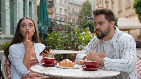 Téléchargez les photos : Européen jeune couple dans la ville café femme sourire rire émotionnel texto smartphone ignorer homme fixe regard lointain frustré relation problème indifférence à l'extérieur petit déjeuner addiction Internet - en image libre de droit