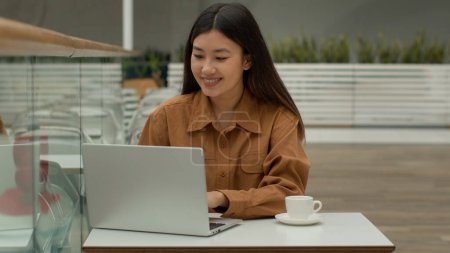 Téléchargez les photos : Asiatique jolie fille chinoise femme d'affaires travailler avec ordinateur portable boisson café coréen japonais femme d'affaires pigiste étudiant tapant sur ordinateur bavarder et sourire occasionnel utilisation de travail wi-fi dans l'espace de travail café - en image libre de droit