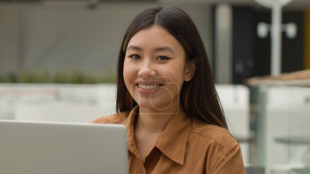 Téléchargez les photos : Heureuse asiatique femme chinoise coréen japonais fille d'affaires travaillant ordinateur portable dans le café multiracial bureau employé navigation site internet entreprise e-commerce regarder la caméra sourire satisfait sourire - en image libre de droit