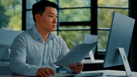 Photo for Professional asian businessman korean japanese 40s man lawyer office worker reading financial documents invoice contract budget documentation searching business data at computer paying bills online - Royalty Free Image