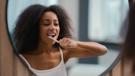 Reflejo en espejo Mujer afroamericana sosteniendo cepillo de dientes cepillado dientes blancos biracial chica limpieza femenina boca higiene bucal procedimiento cuidado dental matutino rutina blanqueamiento dental con cepillo