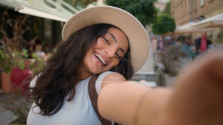 Happy positive smiling teen tourist traveler woman Indian Arabian ethnic female girl student taking selfie photo posing outside abroad city street cafe. Holidays memories vacations weekend relaxation