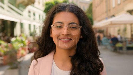 Foto de Cerca de retrato adolescente indio árabe mujer étnica chica estudiante mujer de negocios abrir lentamente los ojos mirando a la cámara dientes blancos sonriente motivación relajante recreación fuera de la calle de la ciudad - Imagen libre de derechos