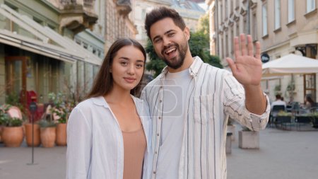Young Caucasian European happy family man woman smiling greeting advertising clinic invite welcome client coming closer inviting hand city outdoors street sign gesture toothy dental smile couple hug
