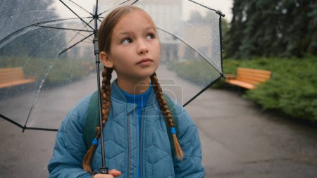 Photo for Dissatisfied little girl city street outside bad weather rain schoolgirl with umbrella learner school unhappy child kid pupil autumn park annoyed displeased disappointed expression sad upset education - Royalty Free Image