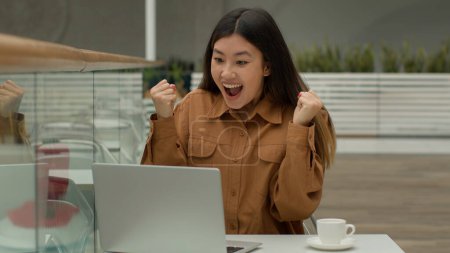 Téléchargez les photos : Heureuse choquée femme d'affaires asiatique assis dans un café avec ordinateur portable surprise coréenne fille gagnante gagner offre d'emploi célébrer enchère internet gagner prix en ligne crier se réjouir victoire succès surprise - en image libre de droit