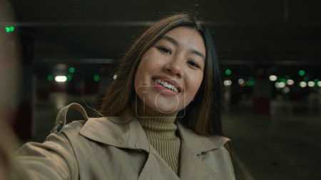 Téléchargez les photos : Webcam view POV heureux sourire asiatique femme fille chinois coréen blogueur vlogger influenceur parler à smartphone caméra pour canal de blog social blogging histoire tenir téléphone portable enregistrement vidéo dans le parking - en image libre de droit