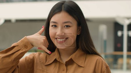 Foto de Close up Mujer asiática sonriendo japonés chino coreano chica mujer de negocios señalando el dedo a la cámara haciendo gesto de teléfono hey me llamas de nuevo propuesta de conversación de llamar al número de contacto del teléfono celular - Imagen libre de derechos