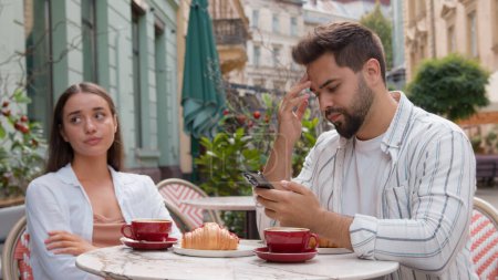Photo for Caucasian couple eat breakfast in city cafe outdoors addicted busy man boyfriend using mobile phone ignoring upset woman girlfriend offended arms crossed quarrel crisis relationship problem conflict - Royalty Free Image