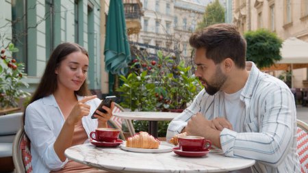 Photo for European young couple in city cafe woman smiling laughter emotional texting smartphone ignore man fixed gaze distant frustrated relationship problem indifference outdoors breakfast internet addiction - Royalty Free Image