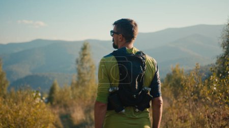 Photo for Back view thoughtful calm adult Caucasian male man guy sportsman mountaineer athlete rest hiking looking around enjoy atmosphere sport healthy lifestyle contemplating nature high mountain hill outside - Royalty Free Image