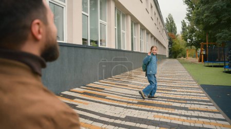 Photo for Father walk daughter to school family tender relations goodbye wave hand learner schoolgirl little girl pupil education kid schoolbag child protecting affectionate support parenthood care city outside - Royalty Free Image