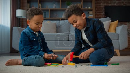 Photo for Two ethnic little boys African American multiracial kids schoolboys pupils children play game sitting on carpet in living room indoors at home brothers friends playing with plastic toys repair tools - Royalty Free Image