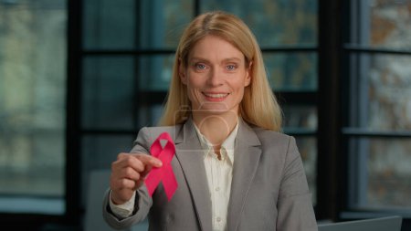 Téléchargez les photos : Portrait souriant Une femme d'âge moyen caucasienne tient un ruban rouge posant dans un bureau moderne femme d'affaires séropositive signe de prévention de la maladie signe bénévolat symbole de charité. Journée mondiale du cancer du sein - en image libre de droit