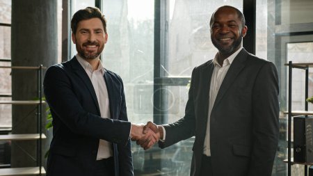 Photo for Two diverse multiracial businessmen business colleagues partners men handshaking in office posing smiling to camera Caucasian man and African American employee shaking hands agreement deal partnership - Royalty Free Image