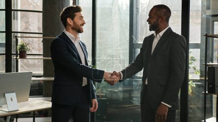 Two diverse men multiracial businessmen talking in office shake hands after successful negotiations. Caucasian man seller handshake African American business partner client partnership deal agreement