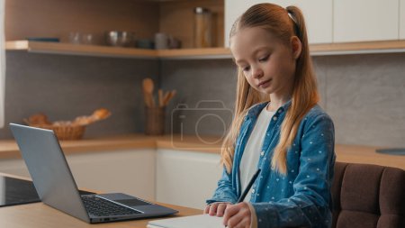 Photo for Caucasian kid girl school pupil studying online from home watching laptop web class lesson teacher by video call e-learning pandemic isolation writing homework task at kitchen child remote education - Royalty Free Image