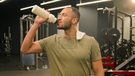 Photo for American Latino man athlete smiling throw towel on shoulder fit sport guy fitness personal trainer instructor male bodybuilder sportsman walking going through gym smile drinking water bottle drink - Royalty Free Image