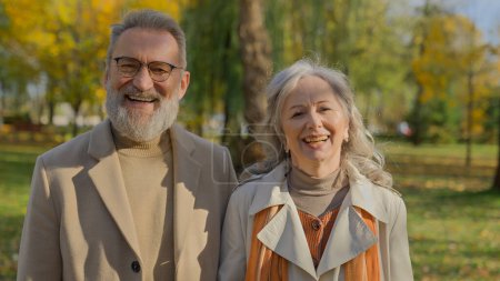 Photo for Portrait of happy mature couple smiling in autumn park cheerful old woman man posing together for camera in nature outdoors elegant senior husband wife retired family laugh have fun love relationship - Royalty Free Image