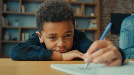 Photo for Sad upset lazy unmotivated tired exhausted fatigued little African American pupil schoolboy writing notes write homework task lying on table. Ethnic child boy kid son at desk boring class home lesson - Royalty Free Image