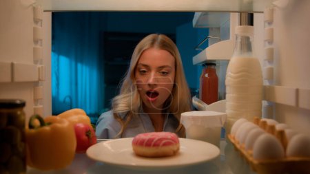 Photo for Point of view POV from inside refrigerator hungry Caucasian woman excited wonder amazed girl at night evening kitchen open fridge sweet donut unhealthy nutrition obesity diet failure food addict - Royalty Free Image