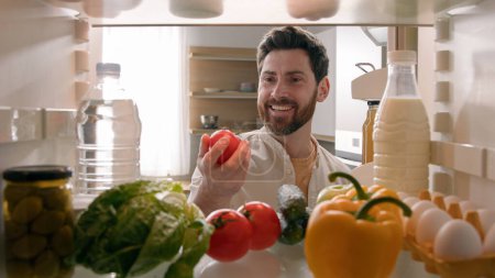 Point of view from inside refrigerator POV Caucasian man householder homeowner open fridge door kitchen full of products food smiling find take red tomato happy smile cooking salad healthy vegetarian