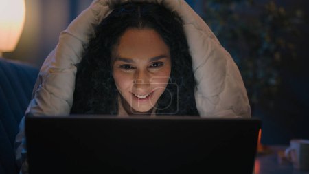 Photo for Smiling happy Hispanic female woman girl Indian Arabian lady smile using computer at late evening night cover under blanket typing on laptop watching movie internet social media addict sleep disorder - Royalty Free Image