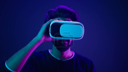 Photo for Metaverse virtual reality cyberspace amazed wonder man take off VR goggles helmet after play game meta universe experience digital technology excited cyber gamer at neon ultraviolet futuristic space - Royalty Free Image