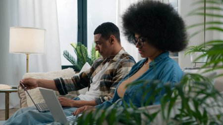 Photo for Busy workers freelancers African American man with woman couple at home couch browsing laptops computers pc devices online internet freelance work remote distant job addiction playing video game apps - Royalty Free Image