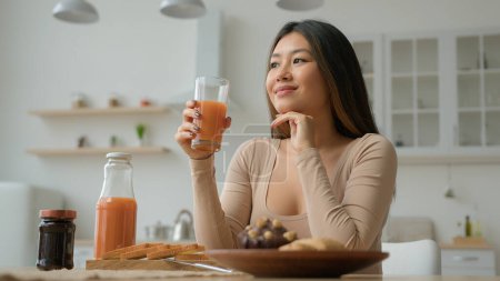 Asiatisch chinesisch lächelnd Frau Koreanisch Mädchen Hausfrau Mutter Frau trinken Orangenpfirsichsaft entspannend trinken Cocktail frische Früchte Smoothie Vitamin Gesundheit Lebensmittel Lieferung genießen Frühstück in der heimischen Küche