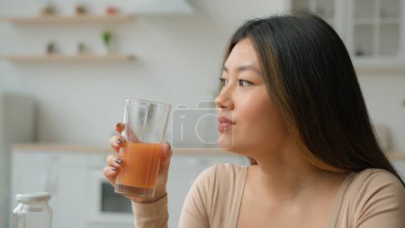 Foto de Mujer coreana bebiendo jugo de naranja batido fresco. Chica vegetariana asiática degustación vaso de vitamina frutal cóctel melocotón bebida dieta saludable pérdida de peso cuidado de la salud nutrición mañana desintoxicación en la cocina - Imagen libre de derechos