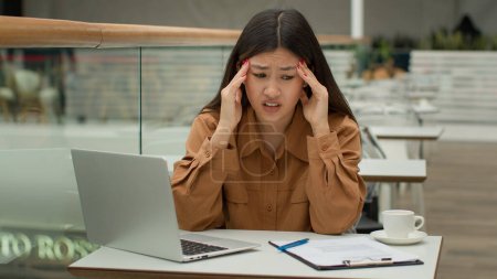 Photo for Stressed tired Asian woman working in cafe with laptop paperwork problem business difficulty sick unhealthy chinese korean businesswoman has painful head headache migraine suffer hurt tension overwork - Royalty Free Image