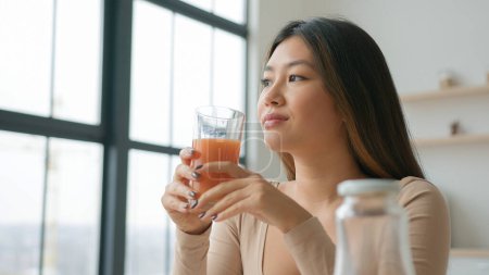 Chinesische Asiatin in der Küche Trinkglas frischer Orangenpfirsichsaft lächelndes Mädchen wegschauen träumen genießen natürliche Früchte Gemüse Smoothie trinken gesunde Erfrischung Gewichtsverlust Entgiftung entspannend