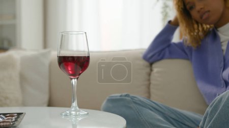 Téléchargez les photos : Pensive détendue rêvant triste calme afro-américain femme alcoolique fille ethnique femme à la maison seul relaxant penser problème prendre verre de vin rouge boisson boire réfléchi regarder verre à vin - en image libre de droit