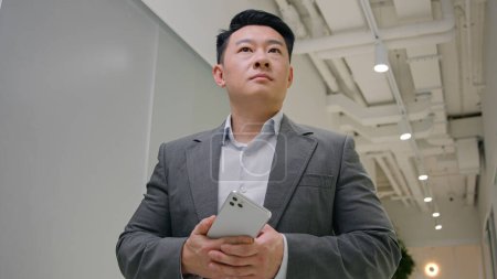 Téléchargez les photos : Réfléchi Asiatique adulte 40s homme d'affaires senior navigation smartphone app mobile chat en ligne affaires réseautage connexions de données chinois coréen japonais homme patron employeur masculin en utilisant Internet par téléphone - en image libre de droit