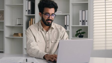 Téléchargez les photos : Arabe homme indien musulman ethnique homme d'affaires employé debout dans le bureau de l'entreprise avec ordinateur portable souriant entrepreneur millénial mâle travaillant en ligne avec des données numériques navigation ordinateur Internet - en image libre de droit