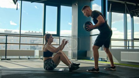 Photo for Personal sport trainer instructor coaching Caucasian girl in gym help motivated sportswoman training on floor exercise with fitness ball throwing use sports equipment healthy strong woman man workout - Royalty Free Image