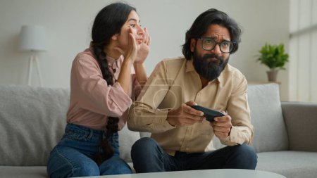 Photo for Indian woman wife distract husband from playing virtual game focused Arabian muslim man addicted play tv console videogame use joystick male funny gamer ignoring overuse gaming ignorance family crisis - Royalty Free Image