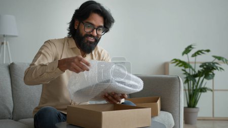 Photo for Happy male customer client consumer Arabian indian man guy in glasses open cardboard box at home unpack online shopping order purchase wrapped package get delivery present gift unpacking carton parcel - Royalty Free Image