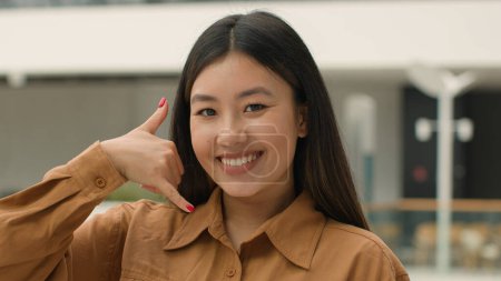 Foto de De cerca mujer asiática feliz sonriente japonés chino coreano chica mujer de negocios mirando a la cámara haciendo gesto de teléfono hey me llamas de nuevo la conversación proposición de llamar al número de contacto del teléfono celular - Imagen libre de derechos