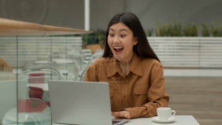 Téléchargez les photos : Heureux surpris asiatique chinois coréen fille d'affaires dans le café gagnant femme gagnant prix sur ordinateur portable pari en ligne célébrer le succès de l'entreprise victoire cri doigt à la publicité site informatique - en image libre de droit